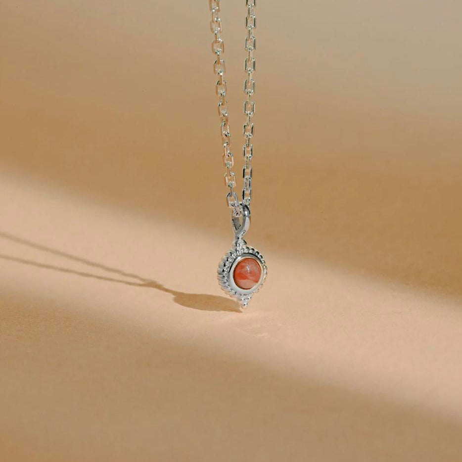 Sterling silver bohemian style necklace hanging with rhodochrosite pink stone displayed against a beige paper background with gentle lighting