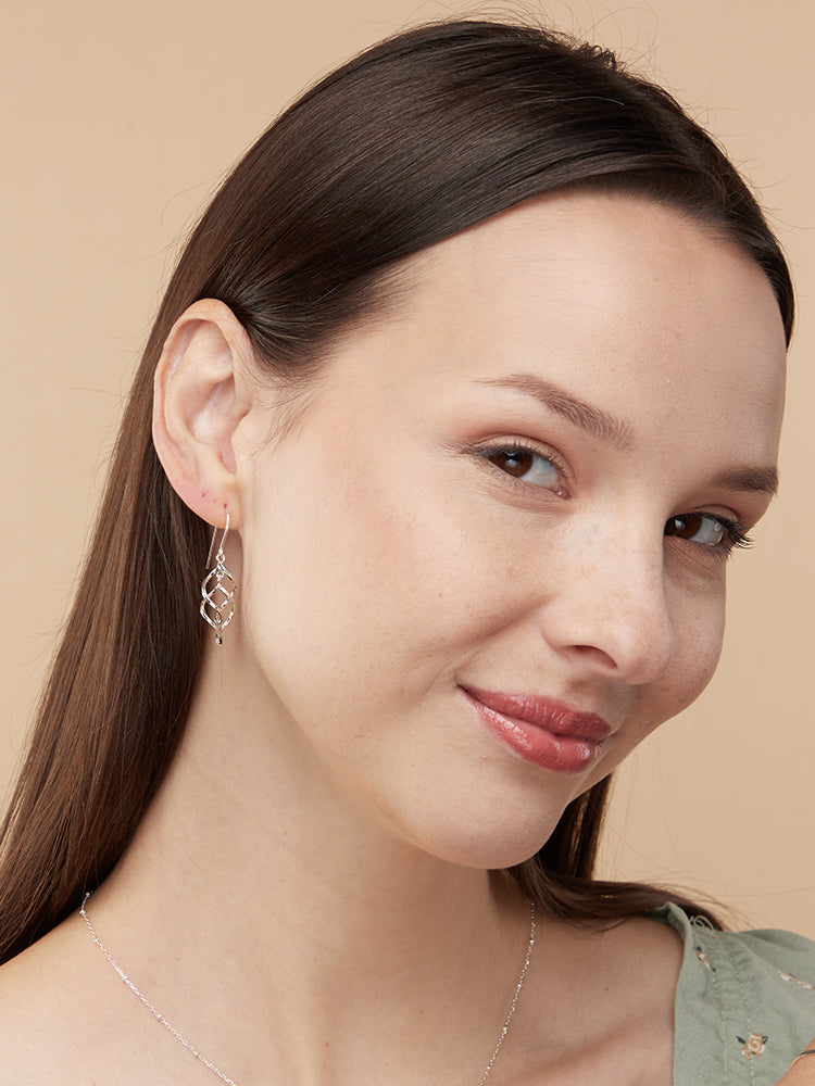 a model with brown hair and head tilted wearing drop dangle sterling silver earrings wearing a green top against a beige background