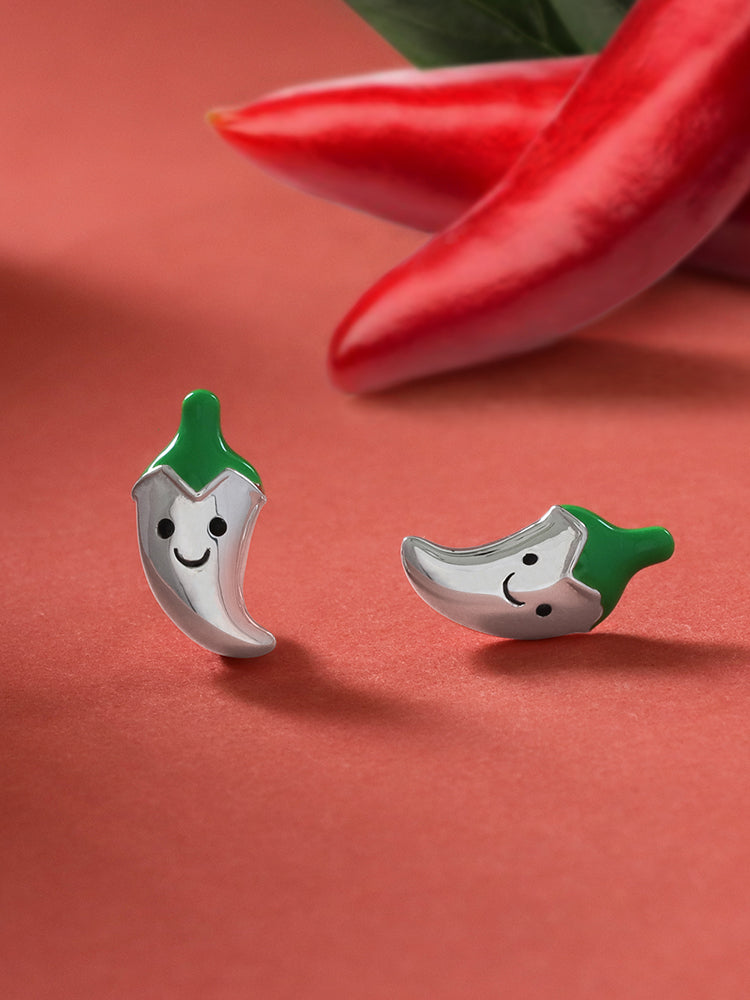 happy chili earring studs in sterling silver with their tops painted in green enamel with a red paper color background and real chilis