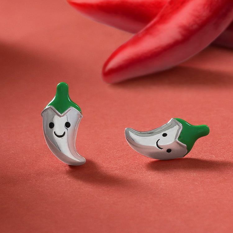 happy chili earring studs in sterling silver with their tops painted in green enamel with a red paper color background and real chilis