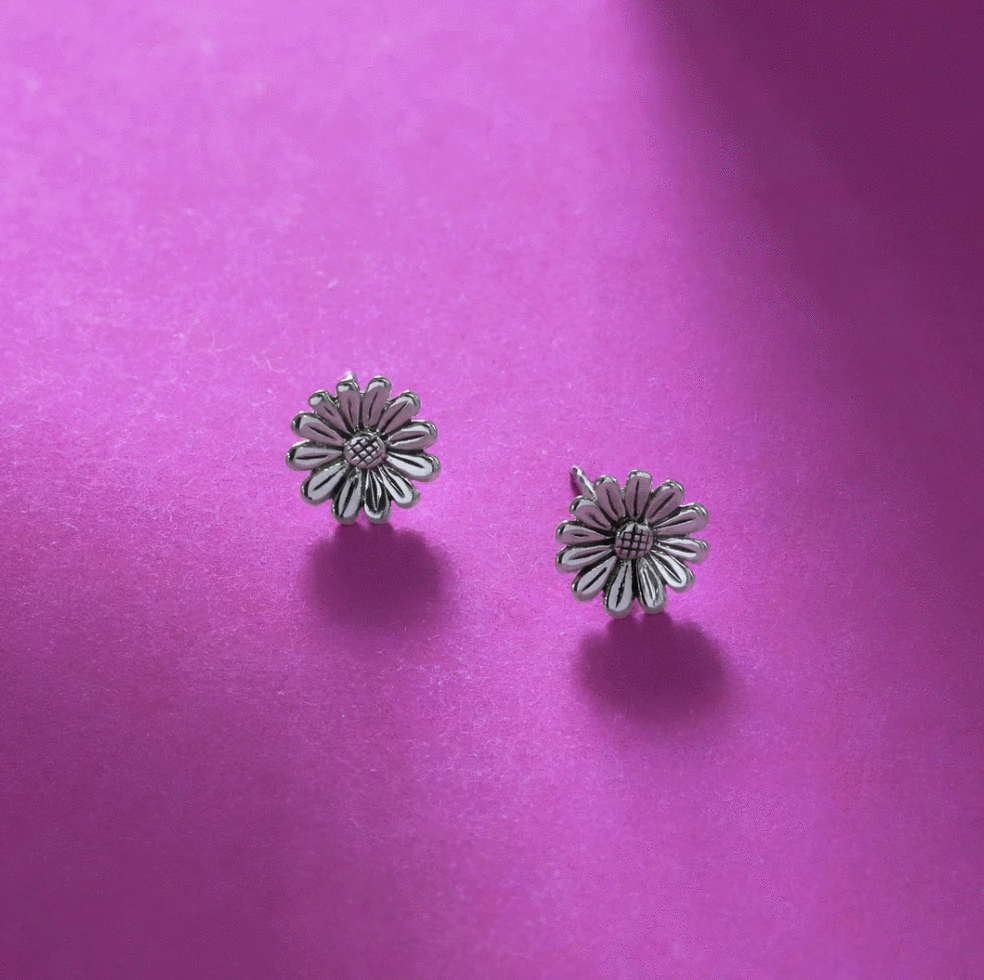 Sterling silver sunflower earring studs with oxidized details displayed against a magenta paper background