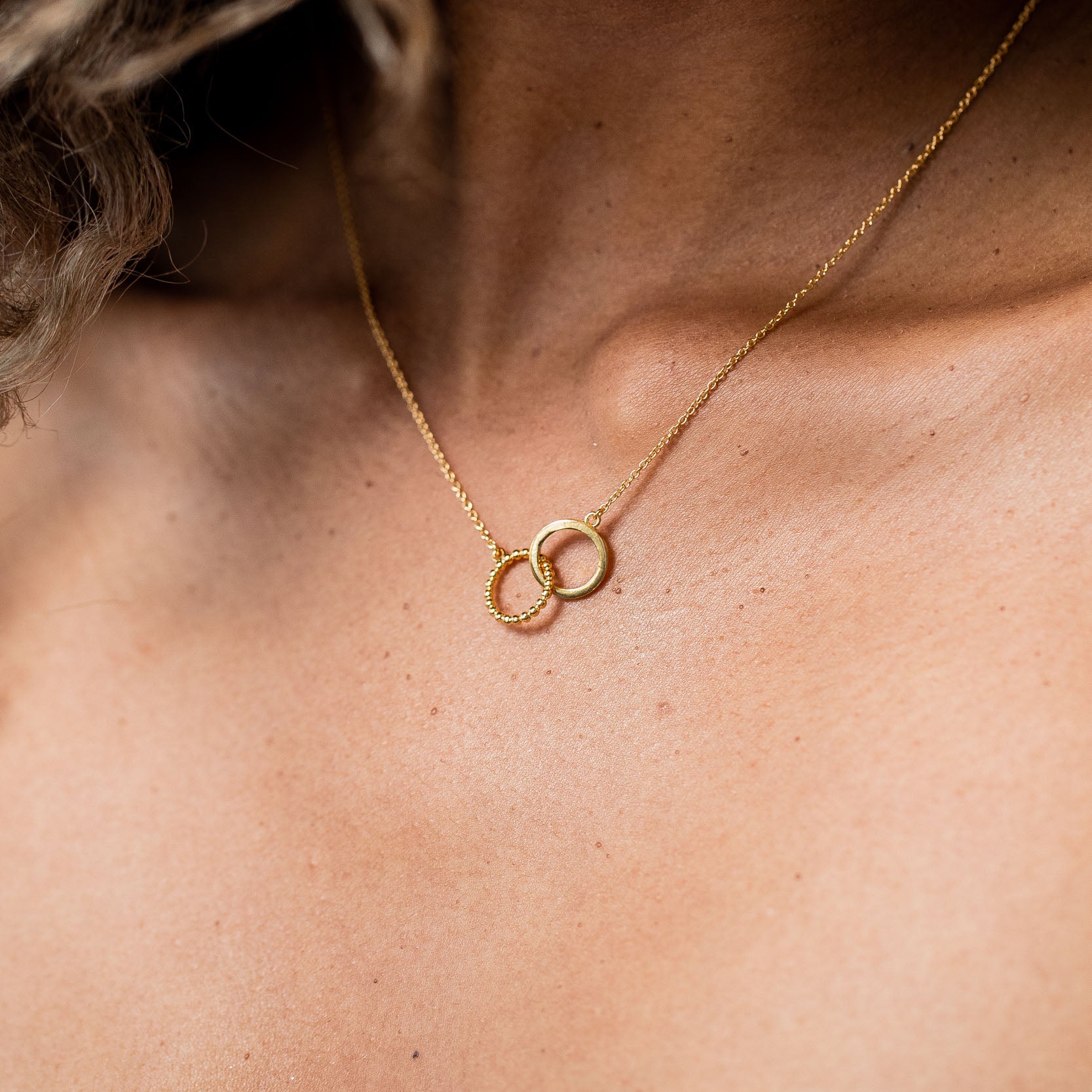 14K Gold Plated Necklace over Sterling Silver with two interlocking circles on model with light brown skin tone